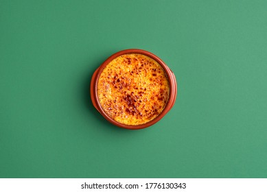 Bowl Of Crème Brûlée With Caramel Crust, In A Clay Tray, On Green Background. Top View Of Homemade Burnt Cream. French Custard Dessert. Caramel Cream