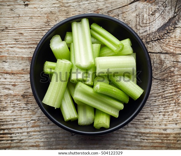 Bowl of\
celery sticks on wooden background, top\
view