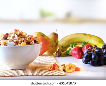 Bowl Of Cereal With Fruit On A White Wooden Table And Fresh Fruits Behind Overview In The Kitchen. Front View