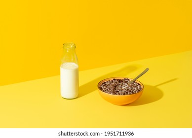 Bowl with cereals and a glass bottle of milk on a yellow table in bright light. Breakfast table with a cereal bowl and a bottle of milk. - Powered by Shutterstock