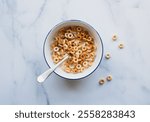 Bowl of cheerios breakfast cereal in milk on white marble.