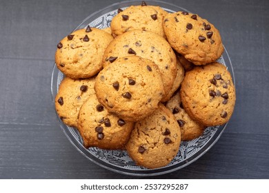 A bowl of chocolate chip cookies with a lot of chocolate chips. The cookies are piled on top of each other, and the bowl is clear - Powered by Shutterstock