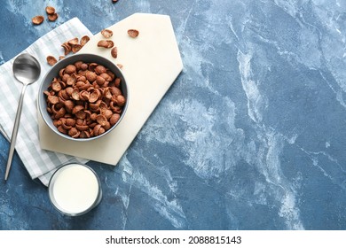 Bowl with chocolate cornflakes and glass of milk on color background