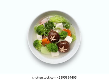 Bowl of clear soup with mix veggy vegetables carrot, brocolli, black shiitake mushrooms tofu. View from top vegetarian vietnamese mushroom clear soup bowl on white background