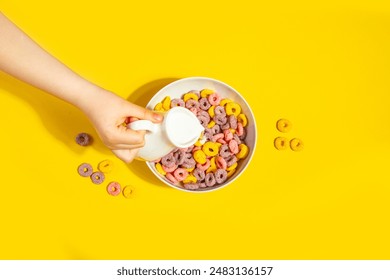 Bowl of colorful cereal corn rings on yellow table. Breakfast concept. Top view. Child kid hand poring milk. - Powered by Shutterstock