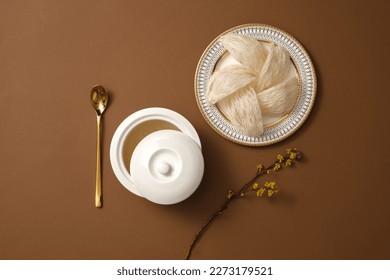 A bowl containing bird’s nest soup decorated with a dish of edible bird’s nest and flower branch on brown background. Bird’s nest can help people sleep well and reduce stress