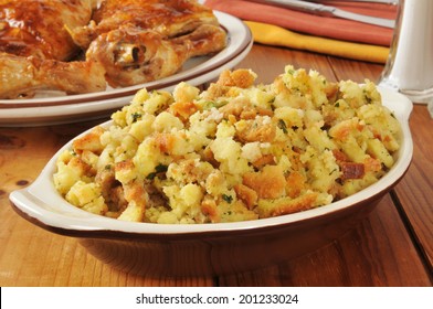 A Bowl Of Corn Bread Stuffing With Rotisserie Chicken In The Background