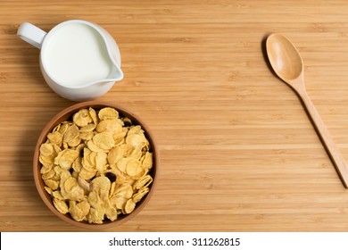 Bowl With Corn Flakes, Jug Of Milk And Wooden Spoon On Table, Top View