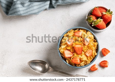 Bowl of corn flakes with sliced strawberries.