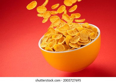 Bowl of corn flakes. Traditional breakfast cereal. Falling cornflakes on red background with copy space