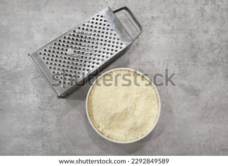 A bowl of Cotija cheese and a stainless steel box grater on the side.
