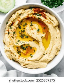 A bowl of creamy hummus topped with chopped parsley and a drizzle of olive oil. The hummus is a light beige color and has a smooth texture