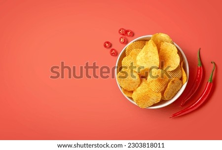 Bowl of crispy wavy potato chips or crisps with chili pepper flavor on red background, top view, empty space for text