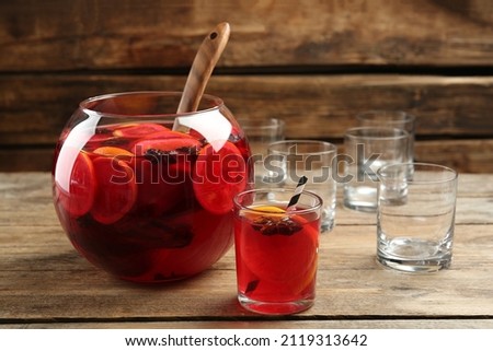 Bowl of delicious aromatic punch drink and glasses on wooden table