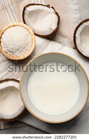 Bowl of delicious coconut milk, flakes and coconuts on light grey table, flat lay