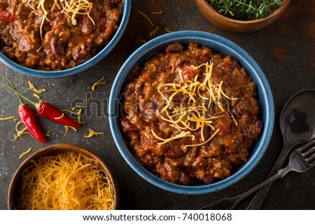 A bowl of delicious home made chili with ground beef, kidney beans, red pepper, tomato and shredded cheddar cheese.