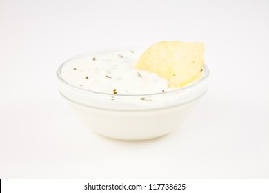 Bowl Of Dip With Herbs With A Chip Dipped In It Against A White Background