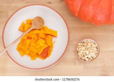 A bowl of dried pumpkin seeds next to a bowl of fresh pumpkin pulp on a wooden tabletop. - Powered by Shutterstock