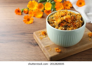 Bowl of dry calendula flowers on wooden table. Space for text