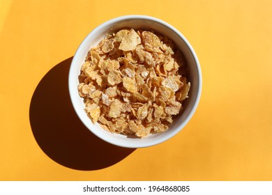 Bowl of dry cornflakes on yellow background. Top view, copy space. Hard light, shadow. Cereal for breakfast