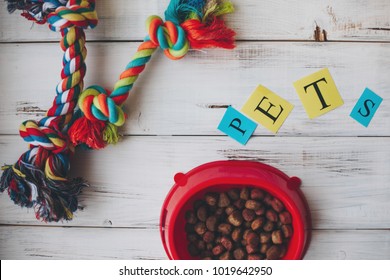 A bowl of dry dog food and rope toy on a white board background. Pet care and veterinary concept. Top view