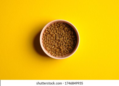 Bowl Of Dry Kibble Cat Food On Yellow Background Top View. Pet Care Concept.