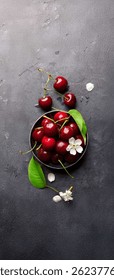 Чаша, наполненная свежей, спелой вишней, а также несколько вишен и вишневых цветов, разбросанных вокруг него. Вишни имеют темно-красный цвет, что указывает на их зрелость.