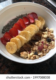 A bowl filled with oatmeal, strawberry milk, strawberry, banana, raisin, granola and chiaseeds.