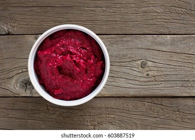 Bowl of fresh beet hummus, above view over a rustic wood background