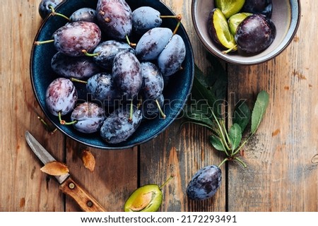 A bowl of fresh blue plums on a wooden background.