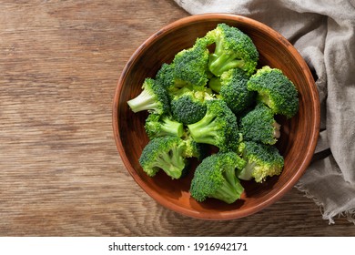 Bowl of fresh broccoli florets on wooden background, top view - Shutterstock ID 1916942171