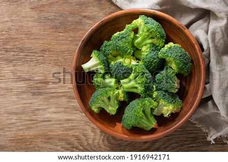 Bowl of fresh broccoli florets on wooden background, top view