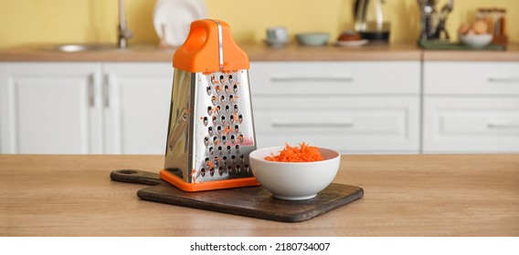 Bowl with fresh carrots and grater on kitchen table