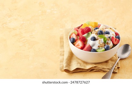 Bowl of fresh fruit salad, muesli and greek yogurt on light yellow background with cotton napkin and spoon. Free space for text.  - Powered by Shutterstock