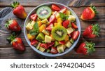 A bowl of fresh fruit salad with strawberries, kiwi, and melon on a wooden table.