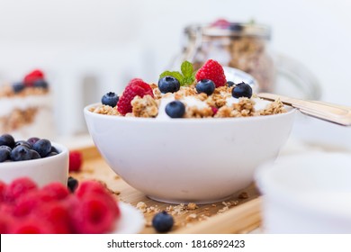 bowl of fresh oat flakes müsli with raspberry and blueberry standing on the breakfast table with fresh milk and a cereals jar in blurry background. summer fitness diet concept.