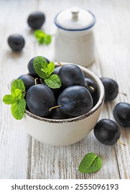 Bowl with fresh plums on a old white wooden table