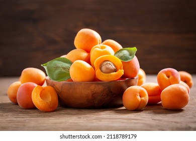 bowl of fresh ripe apricots with leaves on a wooden table
