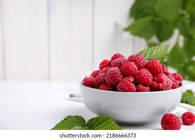 Bowl of fresh ripe raspberries with green leaves on white table against blurred background. Space for text - Powered by Shutterstock