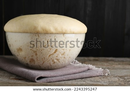 Bowl of fresh yeast dough on wooden table. Space for text