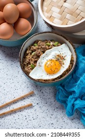 Bowl Of Fried Rice And Mince Topped With A Fried Egg, Studio Shot On A Beige Granite Background, Elevated View