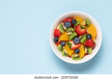 Bowl with fruit salad on blue background. Strawberry, blueberry, kiwi, orange, apple slices. Healthy quick snack concept - Shutterstock ID 2239710185
