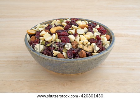 A bowl full of an assortment of nuts and dried cranberries trail mix on a wood table top.