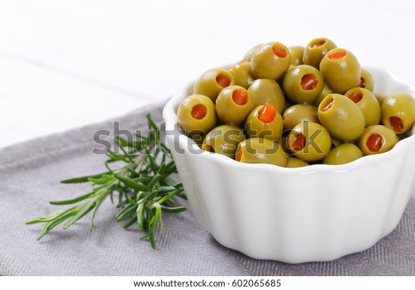 bowl of green olives stuffed with red pepper on grey\
place mat - close up