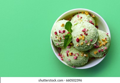 Bowl of green pistachio ice cream and dried fruit pieces isolated on green background. Top view