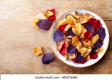 Bowl of healthy colorful vegetable chips on wooden background from top view