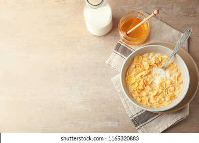 Bowl with healthy cornflakes, milk and honey on light table