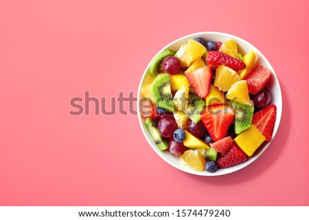 Bowl of healthy fresh fruit salad on pink background, top view