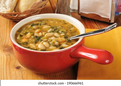 A Bowl Of Healthy Kale And White Bean Soup With Dinner Rolls