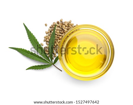 Bowl with hemp oil, leaf and seeds on white background, top view
